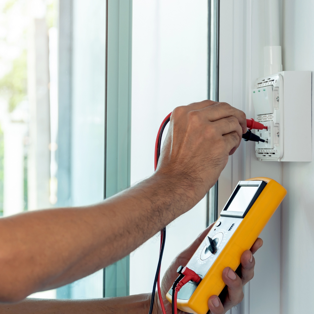 Photo shows a hand holding electrical testing equipment checking a power socket